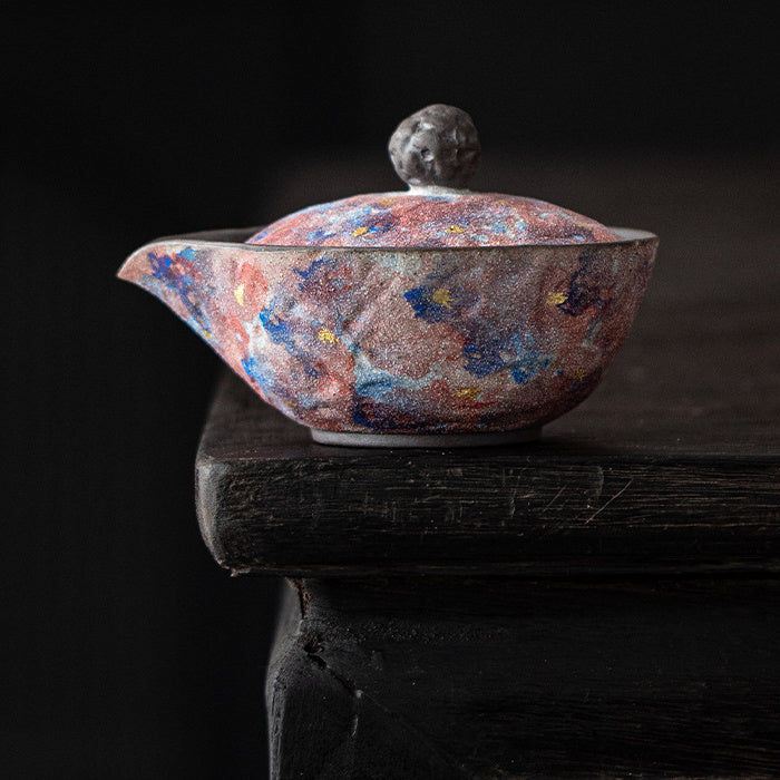 Galaxy glaze handleless ceramic teapot on a dark wooden surface
