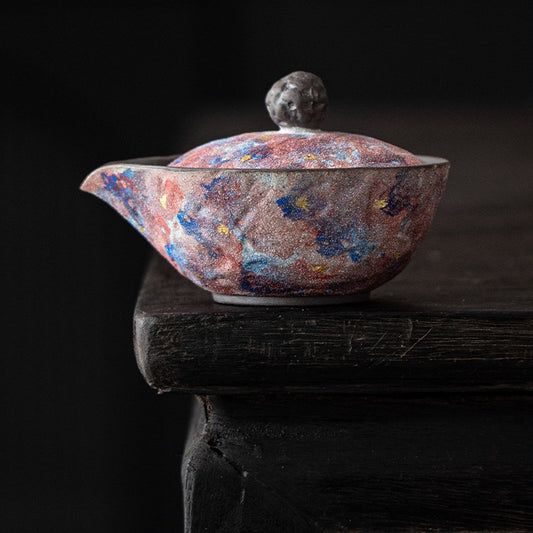 Galaxy glaze handleless ceramic teapot on a dark wooden surface

