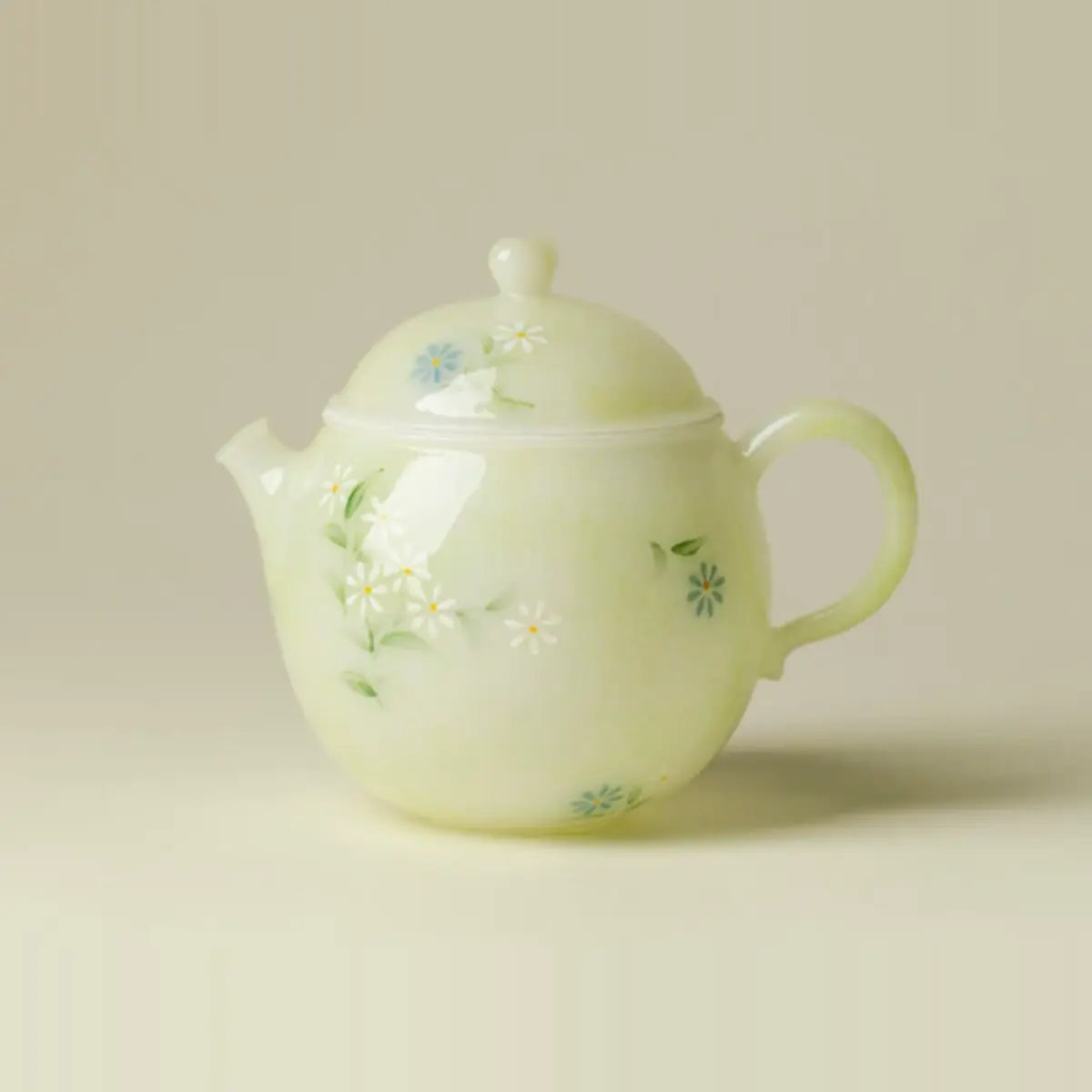 Hand-painted daisy ceramic teapot with a pale jade-green finish on a warm neutral background