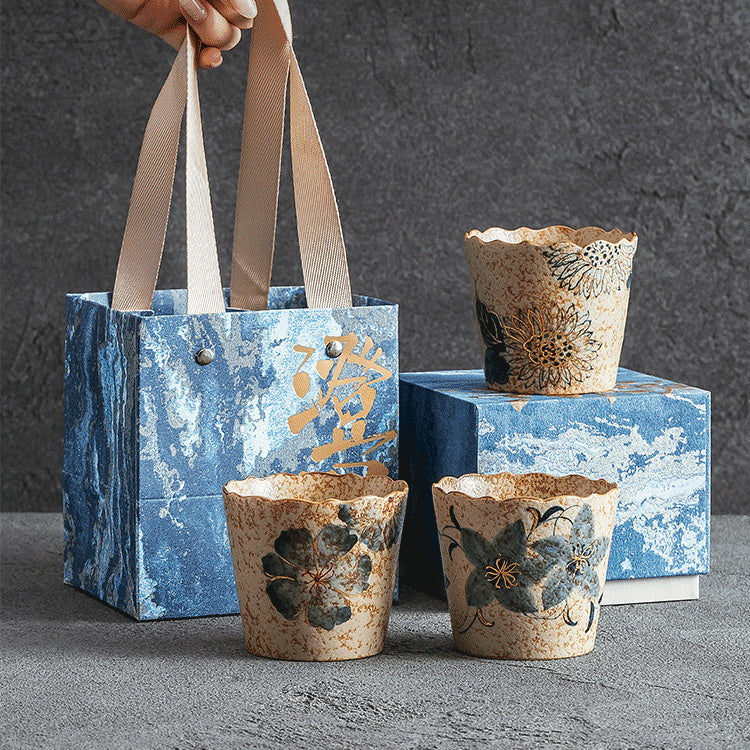 Three hand-painted floral ceramic coffee cups displayed with blue gift packaging
