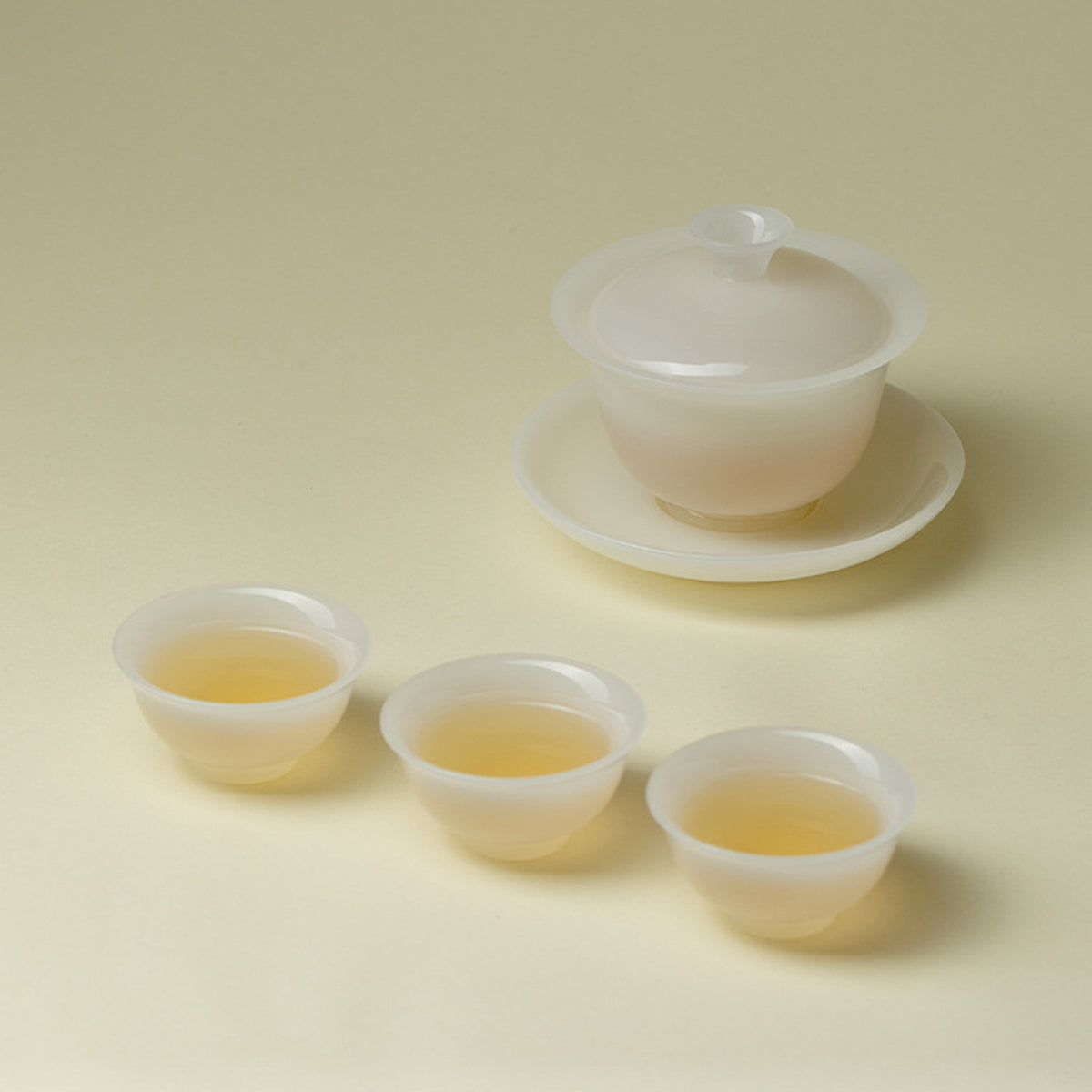 Translucent white ceramic gaiwan tea set with three cups filled with tea
