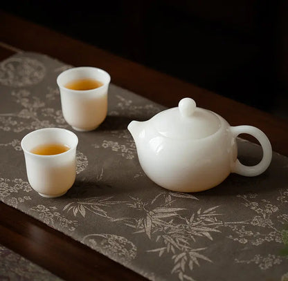 White ceramic Xishi teapot with two matching teacups on a patterned tea mat
