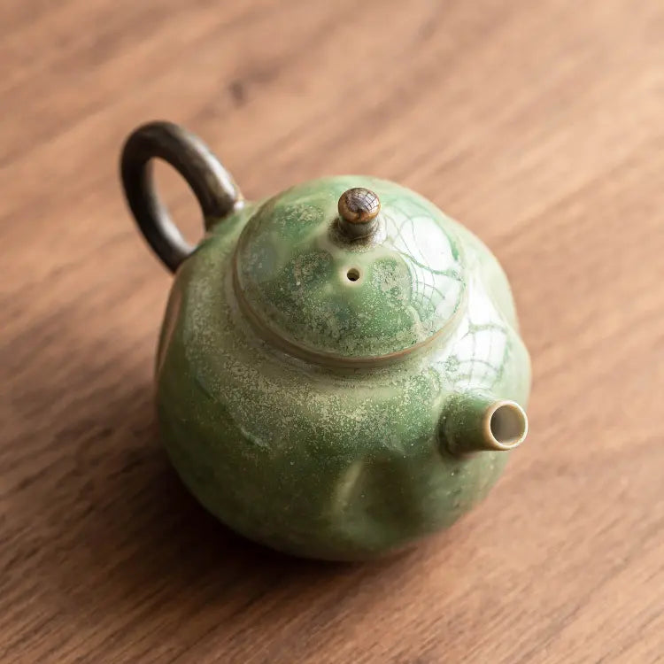 Top-angle view of a green reactive-glaze ceramic teapot on a wooden table
