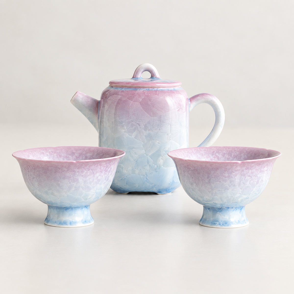 Pink-to-blue crystalline glaze tea set with one softly squared teapot and two matching flower-shaped cups