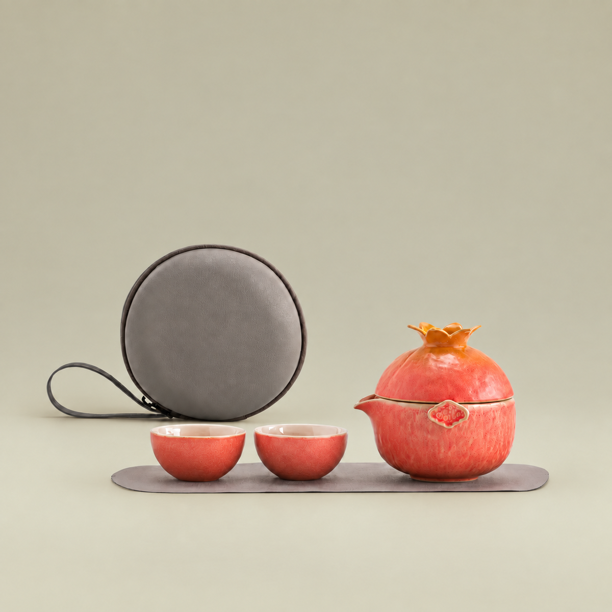 Coral pomegranate ceramic travel tea set displayed with two cups, a round gray carrying case, and white packaging

