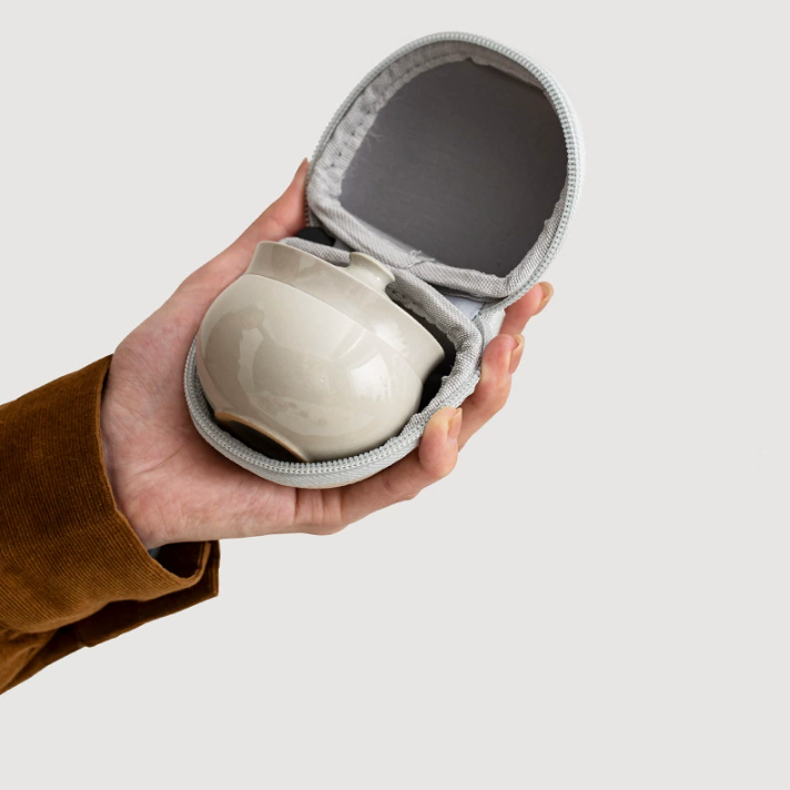 Hand holding an open travel case with the compact gray ceramic tea set nested inside
