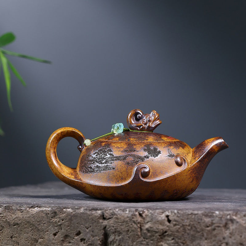 Yixing zisha wood-fired teapot with carved landscape, dragon lid knob, and green bead on a stone display
