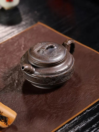 Overhead view of a bamboo drum zisha teapot on a brown tea mat with tea accessories in the background
