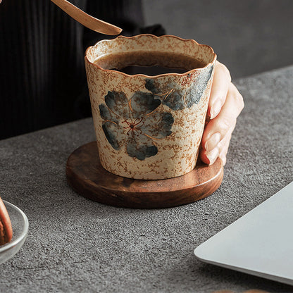 Begonia-pattern hand-painted ceramic coffee cup held beside a laptop on a tabletop
