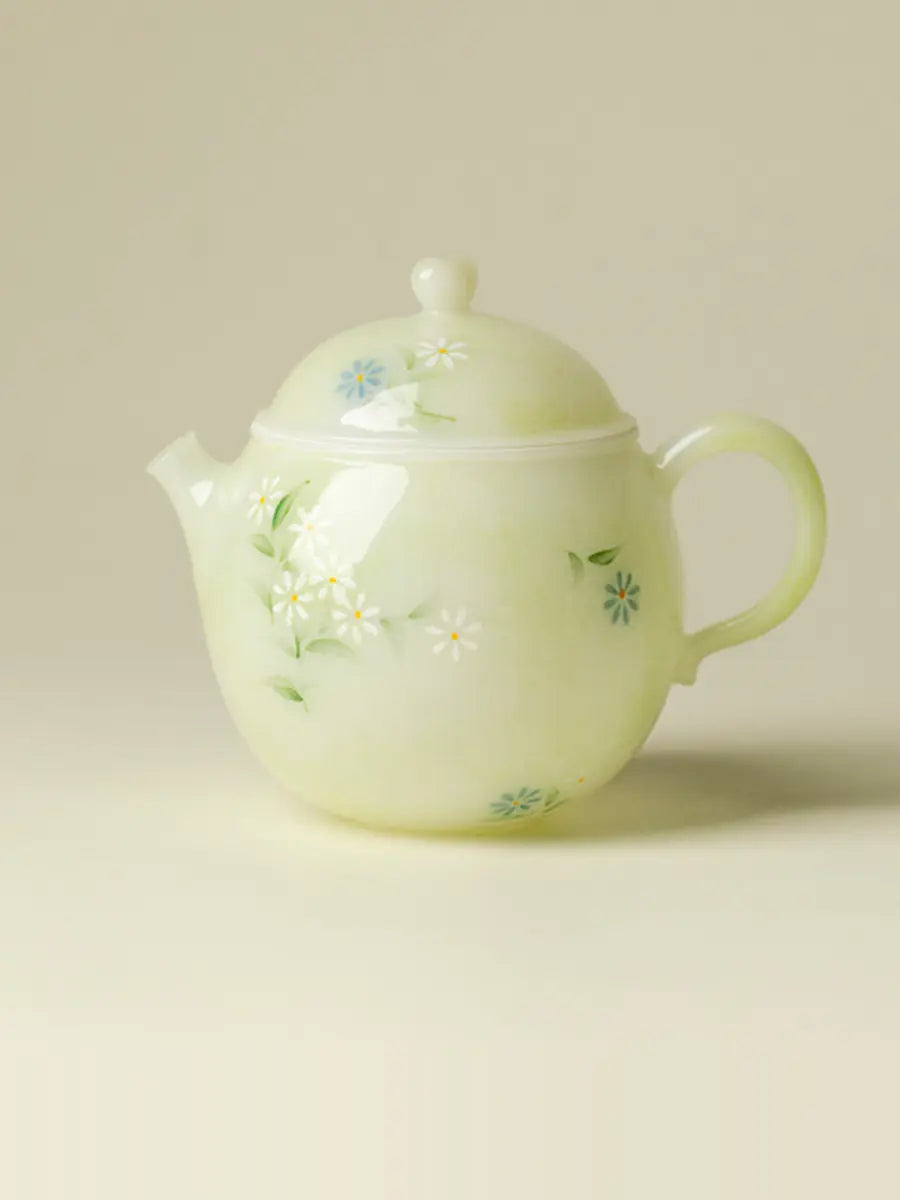 Front view of a small pale green ceramic teapot with white and blue hand-painted daisies