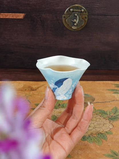 Hand holding a blue whale flower-rim ceramic tea cup filled with tea