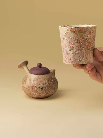 Hand holding the nine-tailed fox ceramic cup with a decorative teapot in the background
