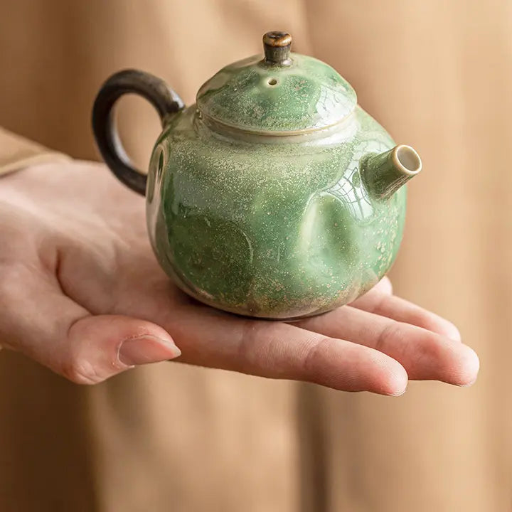 Hand holding a compact green reactive-glaze ceramic teapot to show its scale
