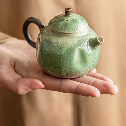Hand holding a compact green reactive-glaze ceramic teapot to show its scale
