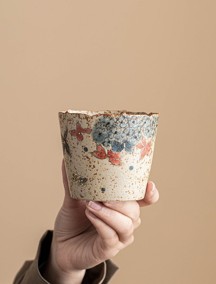 Hand holding the handleless hydrangea ceramic coffee cup against a warm beige background