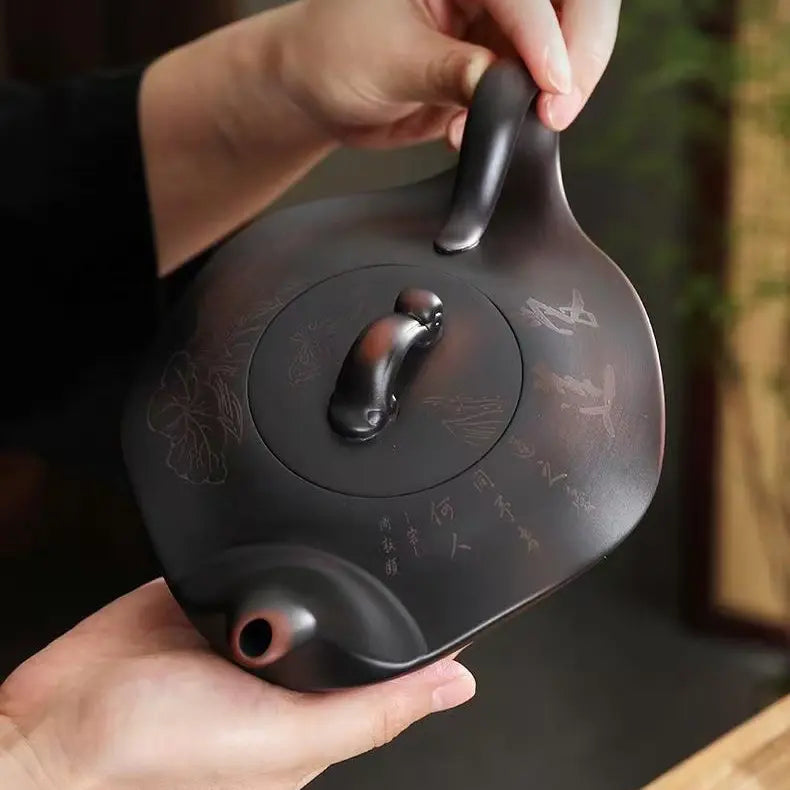 Hands holding the dark brown Yixing zisha teapot from above to show its scale and carved surface