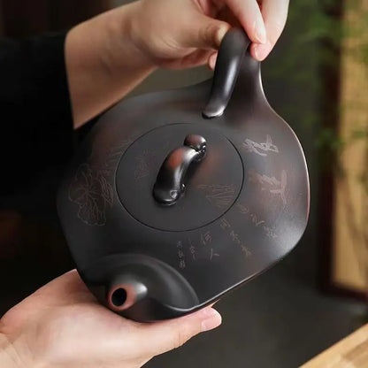 Hands holding the dark brown Yixing zisha teapot from above to show its scale and carved surface
