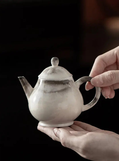 Ink-wash Ruyi ceramic teapot held in two hands against a dark background