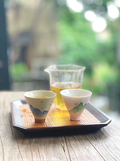Grey-blue mountain relief and pink-green landscape teacups on a tea tray by a bright window