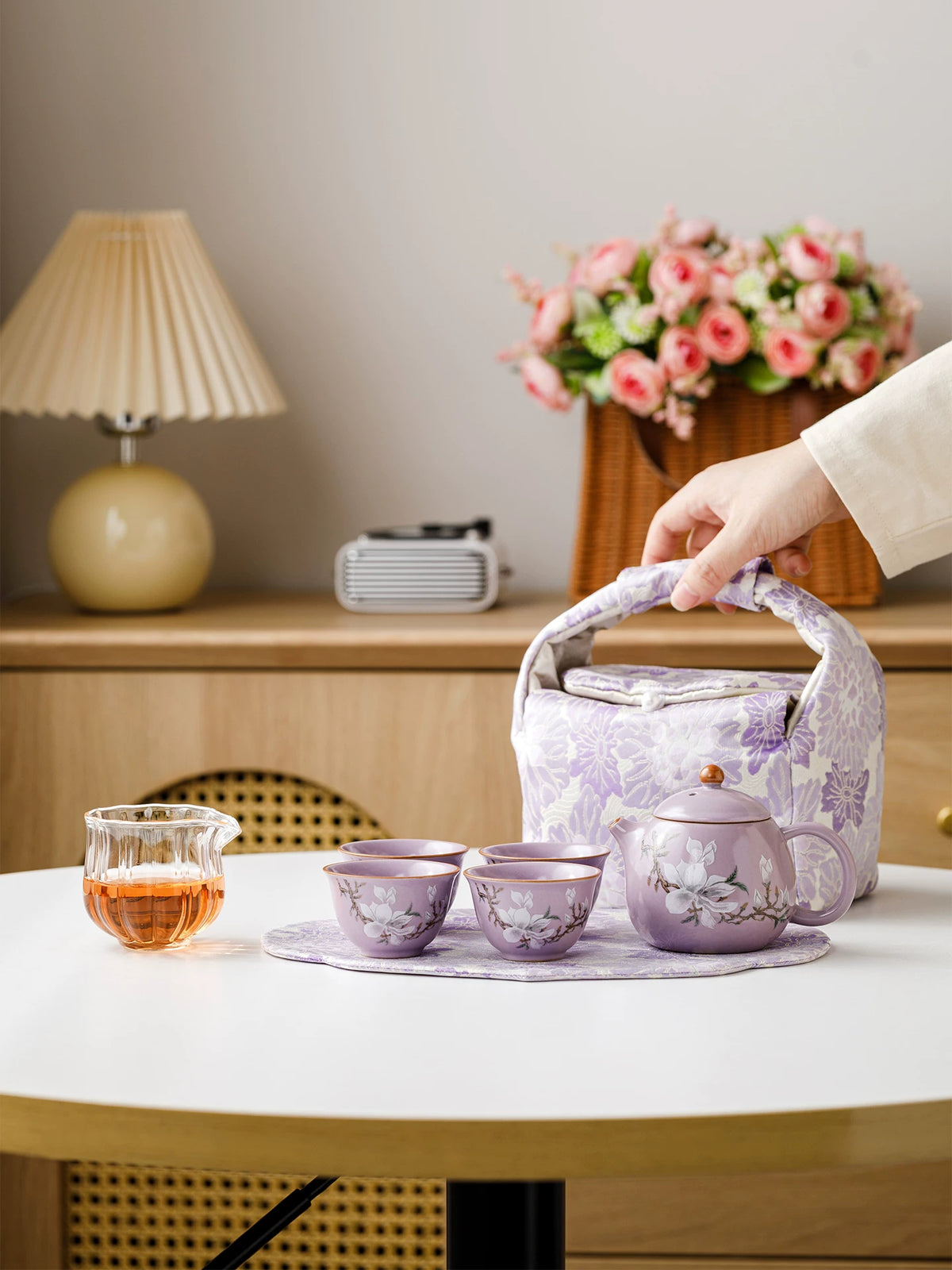 Purple ceramic tea set displayed on a table with its floral travel bag and serving props
