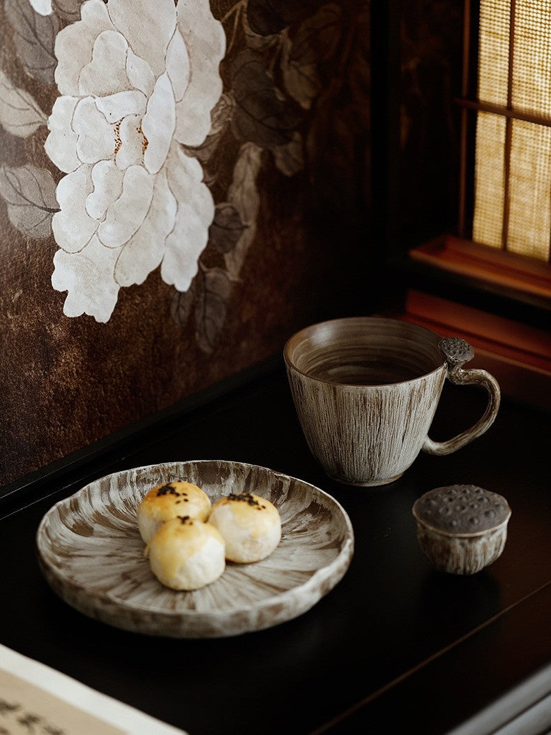 Lotus pod ceramic coffee cup beside a dessert plate with pastries in a dark interior setting