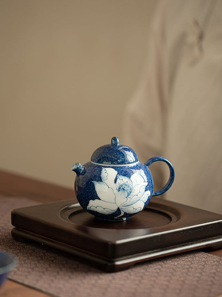 Blue lotus ceramic teapot displayed on a dark wooden tea tray
