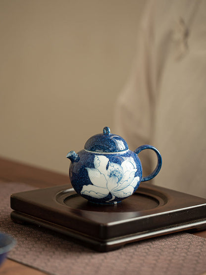 Blue lotus ceramic teapot displayed on a dark wooden tea tray
