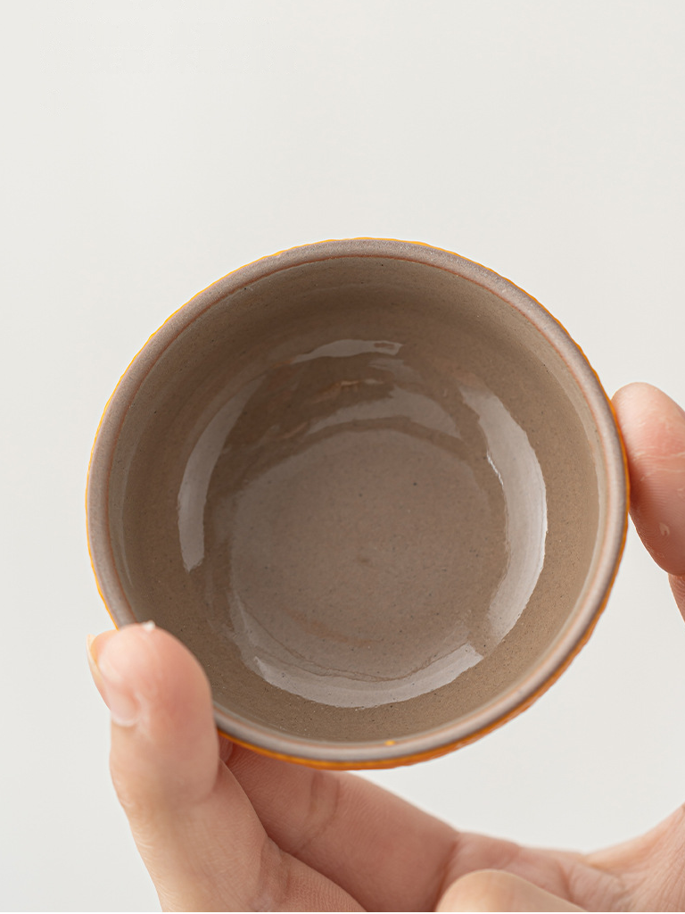 Hand holding a tangerine-shaped ceramic teacup to show its warm neutral glazed interior
