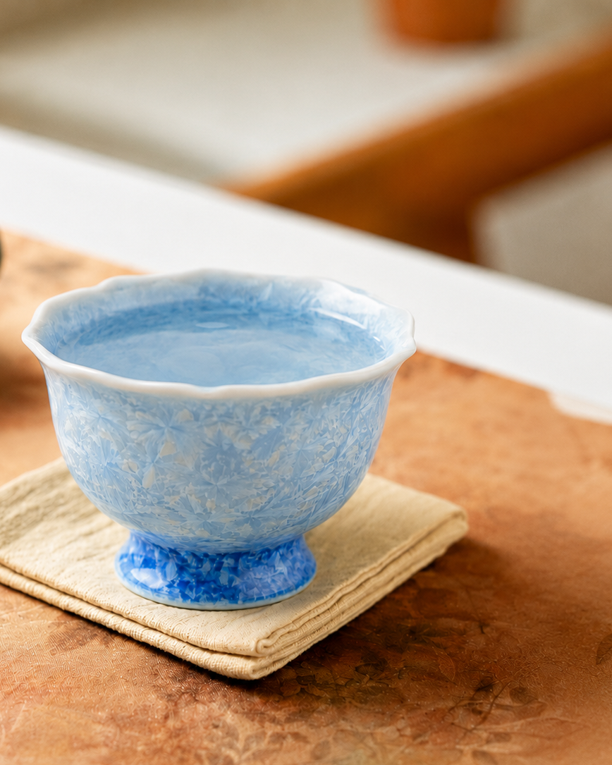 Pale blue crystalline glaze tea cup on folded cloth in a warm tea-table setting