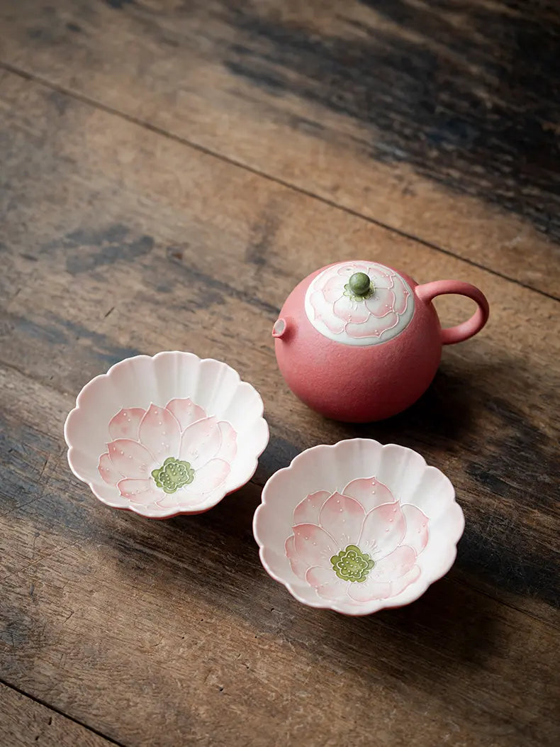Pink lotus ceramic teapot and two flower-shaped teacups arranged on a rustic wooden table
