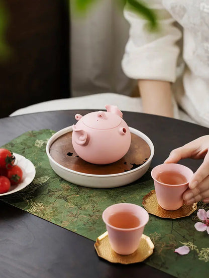 Pink zisha pig teapot and two cups arranged on a tea table
