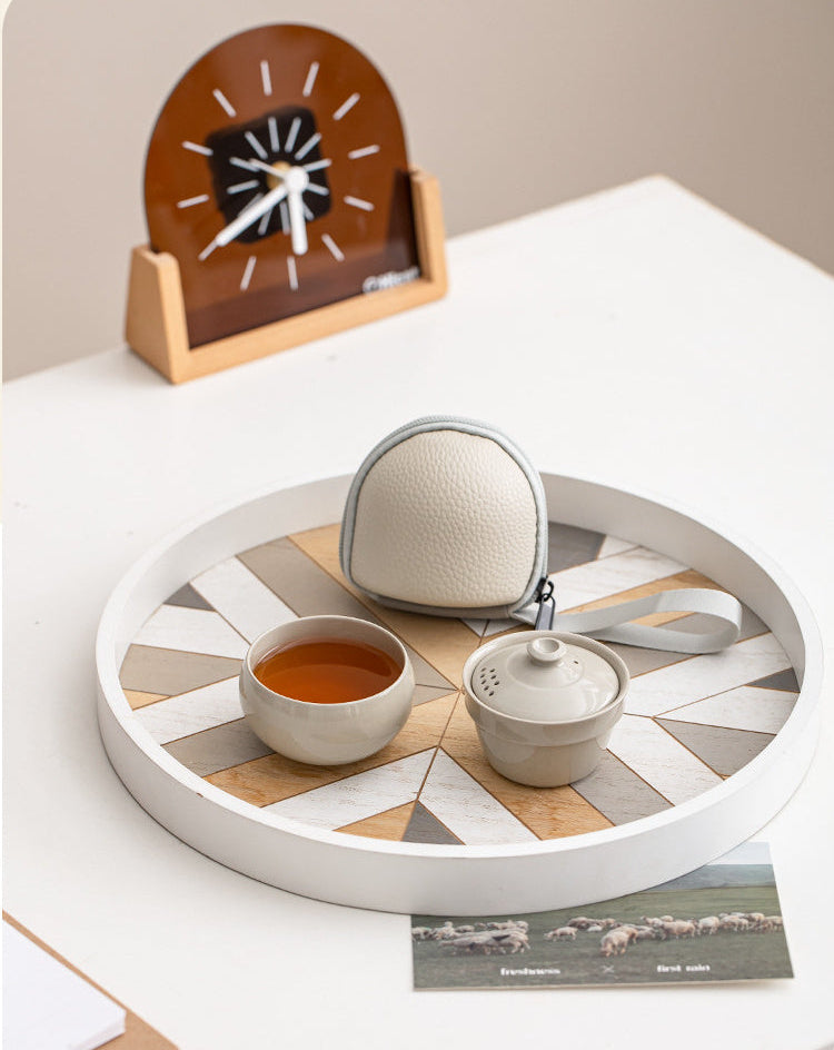 Portable ceramic tea set for one with a tasting cup, lidded brewer, and travel case arranged on a round tray
