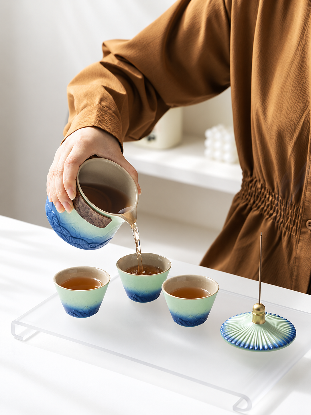 Green and blue ceramic teapot pouring tea into three matching cups
