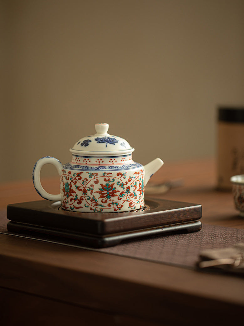 Red and green lotus ceramic teapot displayed on a dark wooden stand