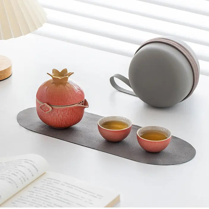 Pomegranate ceramic travel tea set with two cups and a gray carrying case on a sunlit desk
