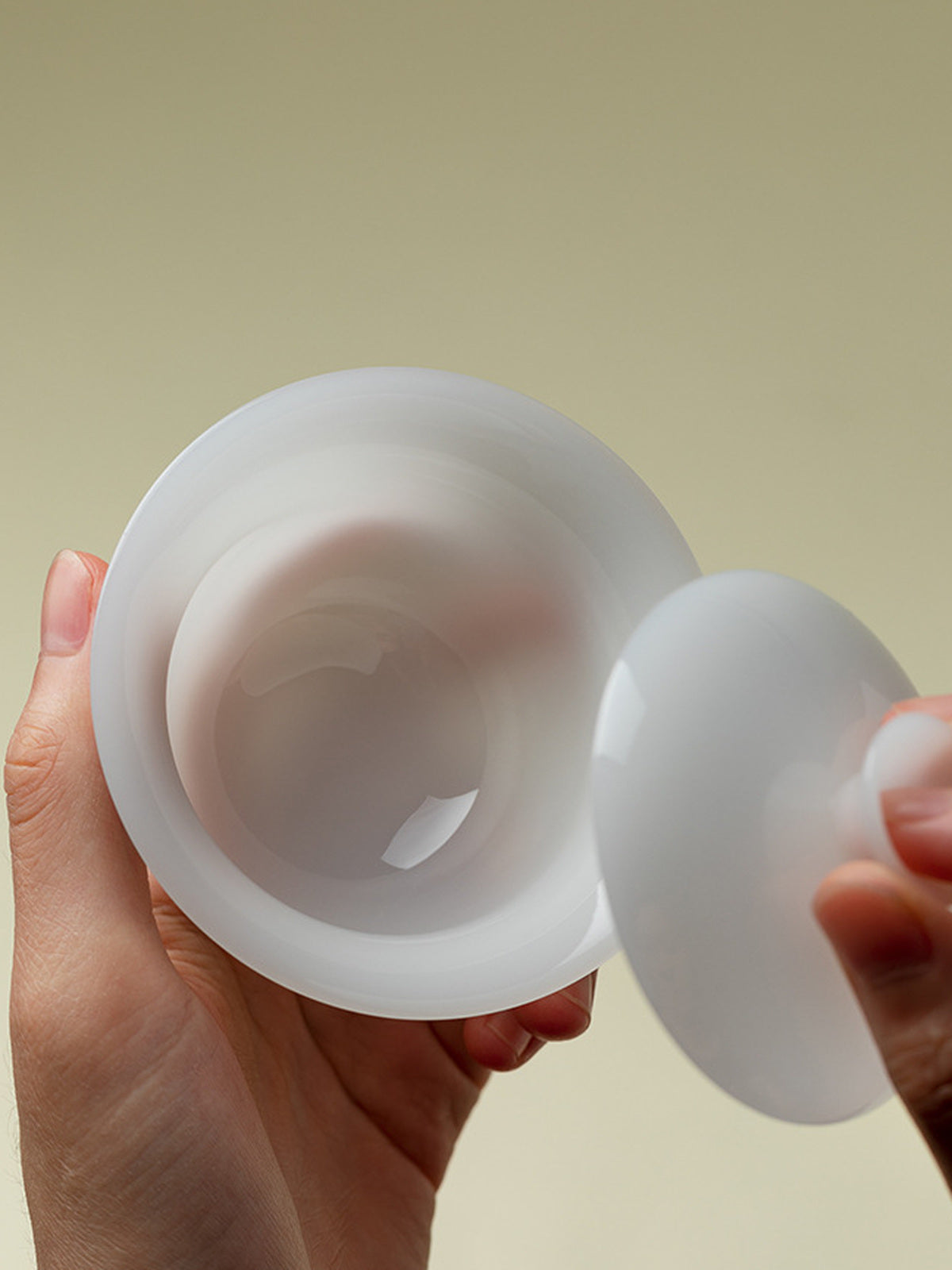 Hands holding a translucent white ceramic gaiwan and its matching lid
