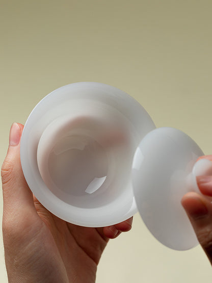 Hands holding a translucent white ceramic gaiwan and its matching lid
