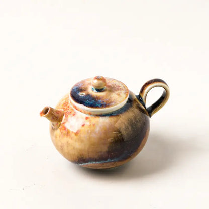 Angled view of the wood-fired ceramic teapot showing its short spout, lid, and ring handle