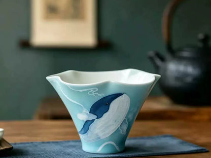Hand-painted blue whale ceramic tea cup displayed on a wooden tea table