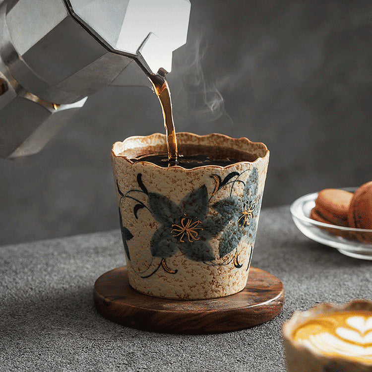 Coffee pouring into a Clock Flower-pattern scalloped ceramic cup on a wooden coaster
