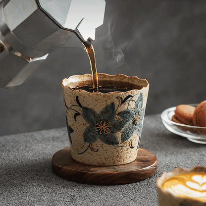 Coffee pouring into a Clock Flower-pattern scalloped ceramic cup on a wooden coaster
