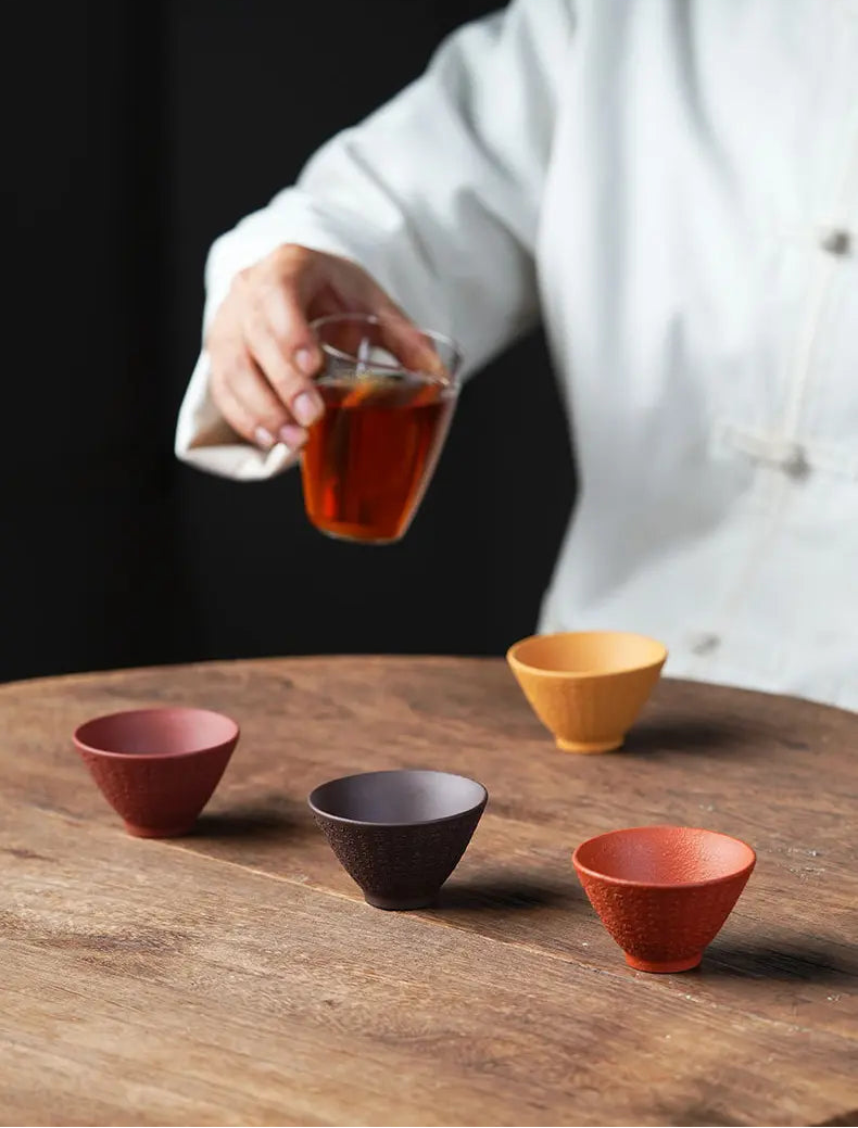 Four earth-tone zisha tea cups on a wooden tea table as tea is served