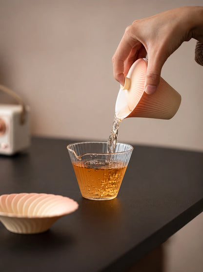 Hand pouring tea from a gradient ceramic gaiwan into a clear ribbed glass pitcher
