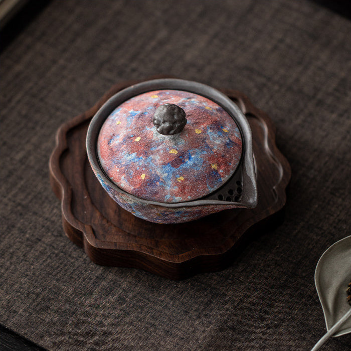 Top view of a galaxy glaze ceramic teapot on a carved wooden tea tray
