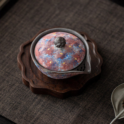 Top view of a galaxy glaze ceramic teapot on a carved wooden tea tray
