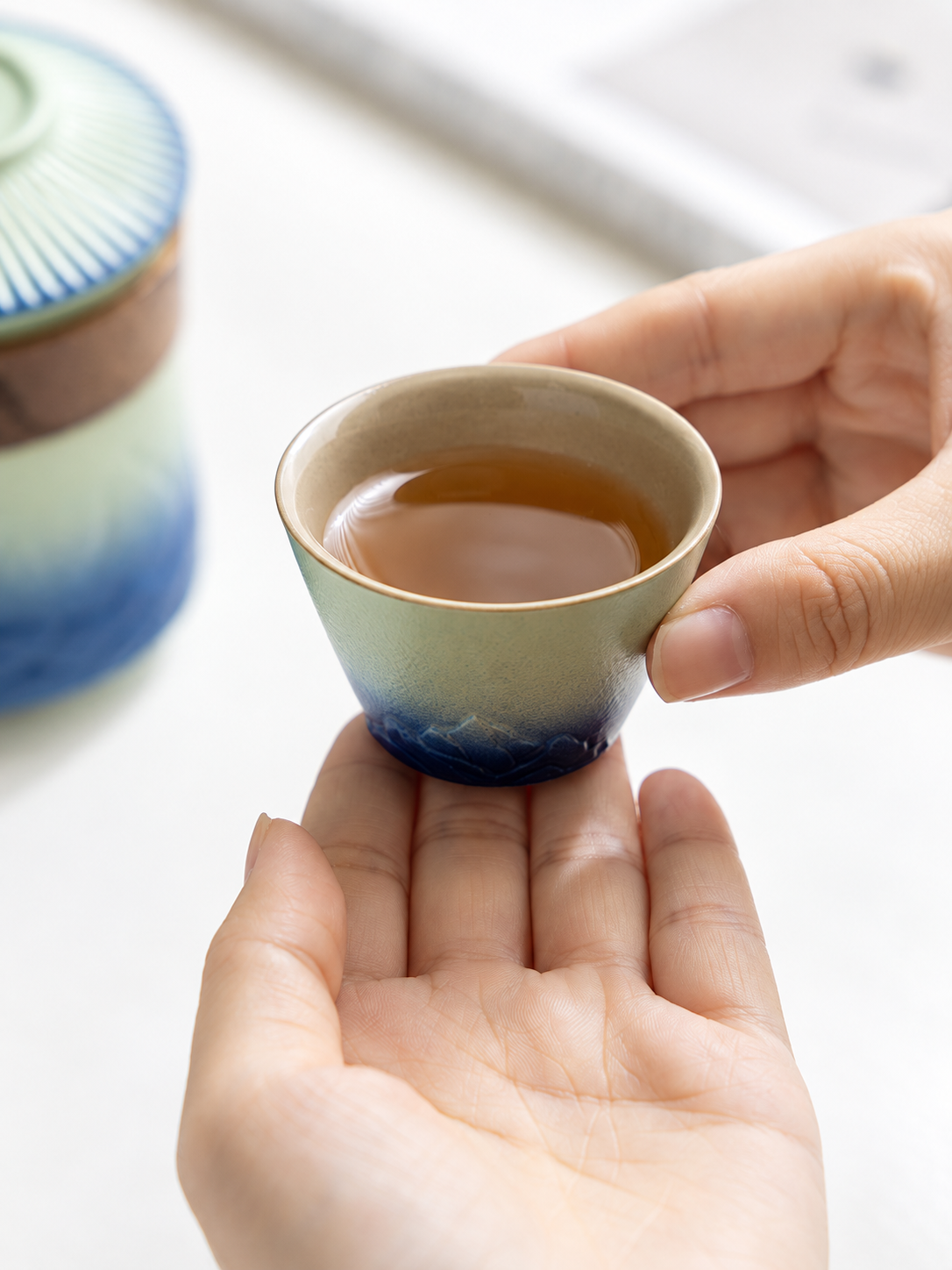 Hand holding a mountain-pattern green and blue ceramic teacup

