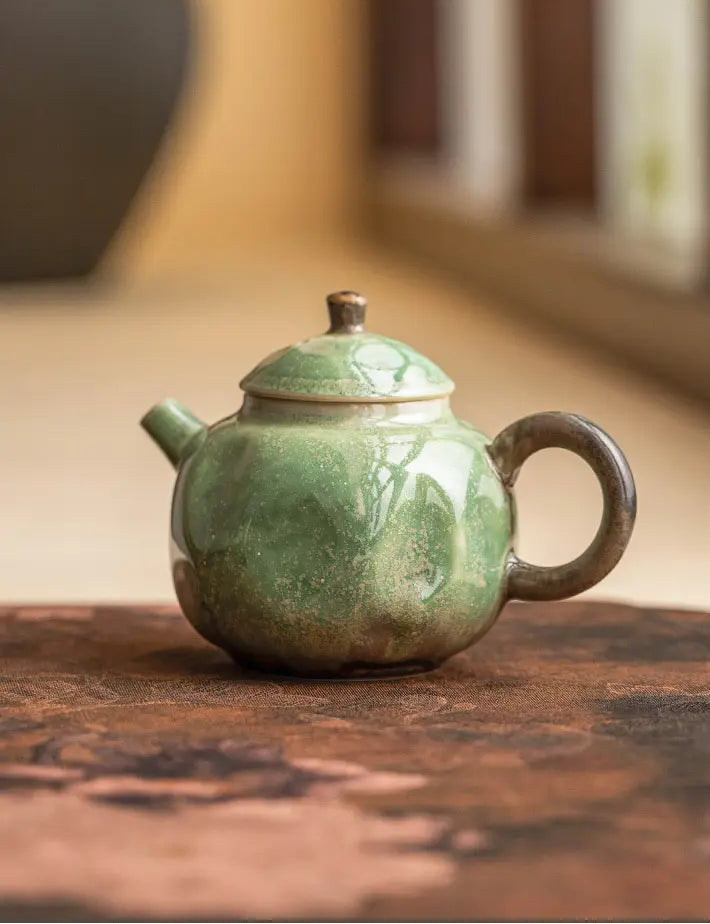 Green reactive-glaze ceramic teapot displayed on a warm wooden tabletop
