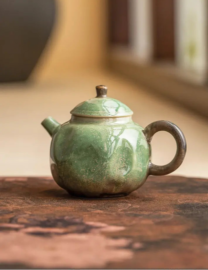 Green reactive-glaze ceramic teapot displayed on a warm wooden tabletop
