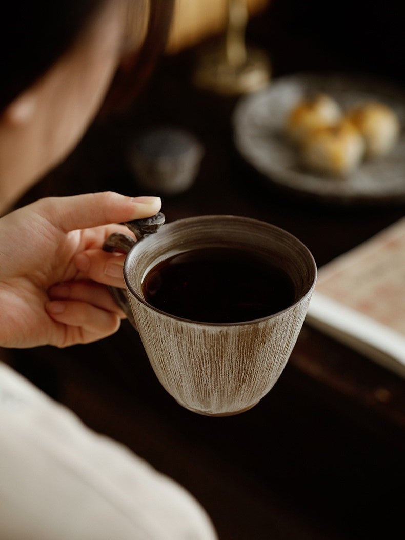 Hand holding a gray-and-white handmade ceramic coffee cup with a sculptural lotus pod handle