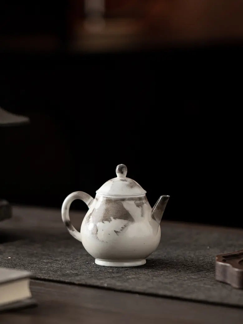 Small ink-wash ceramic teapot displayed on a dark tea table
